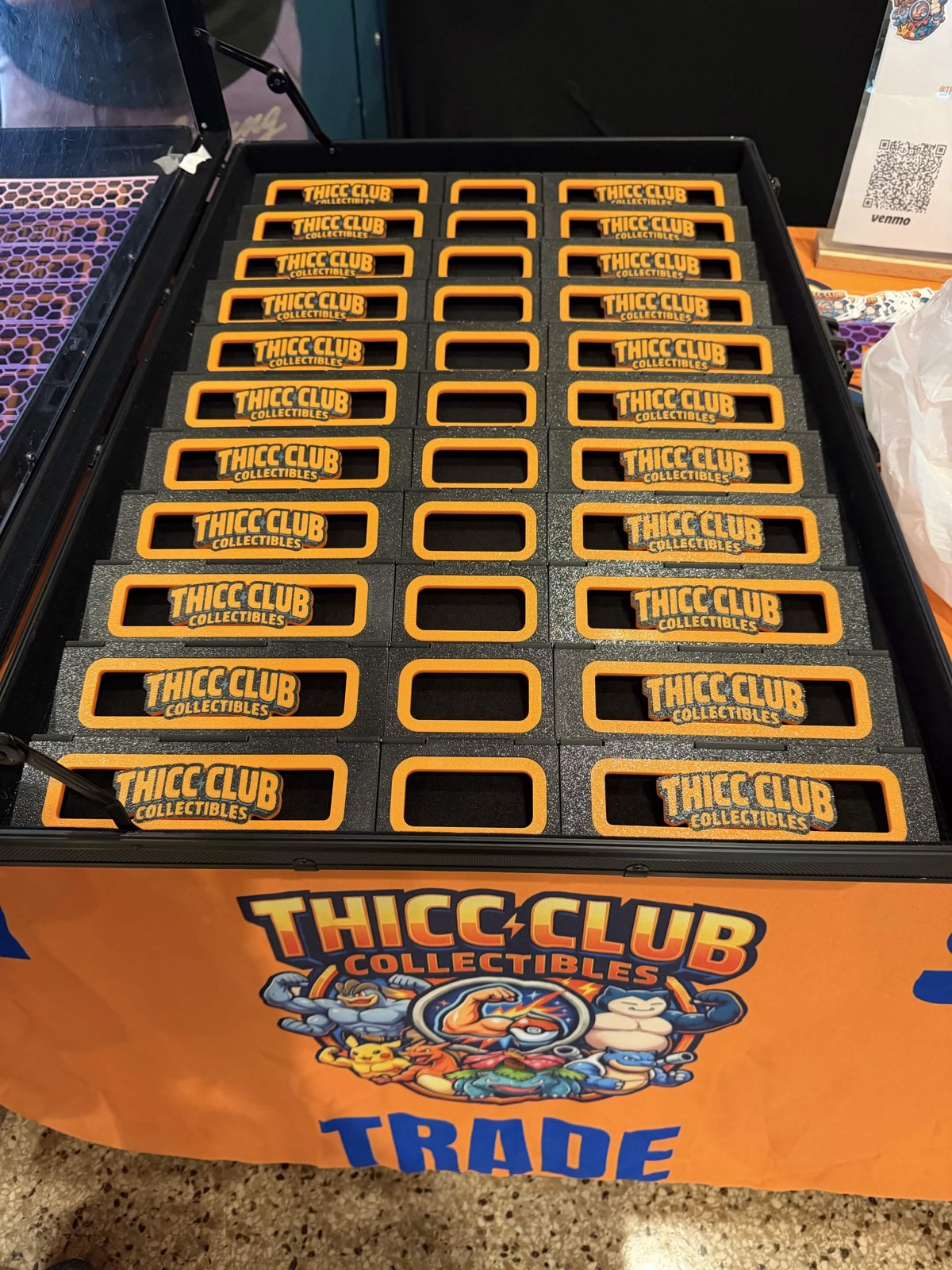 A tray of Thicc Club Collectibles branded risers next to a trade sign